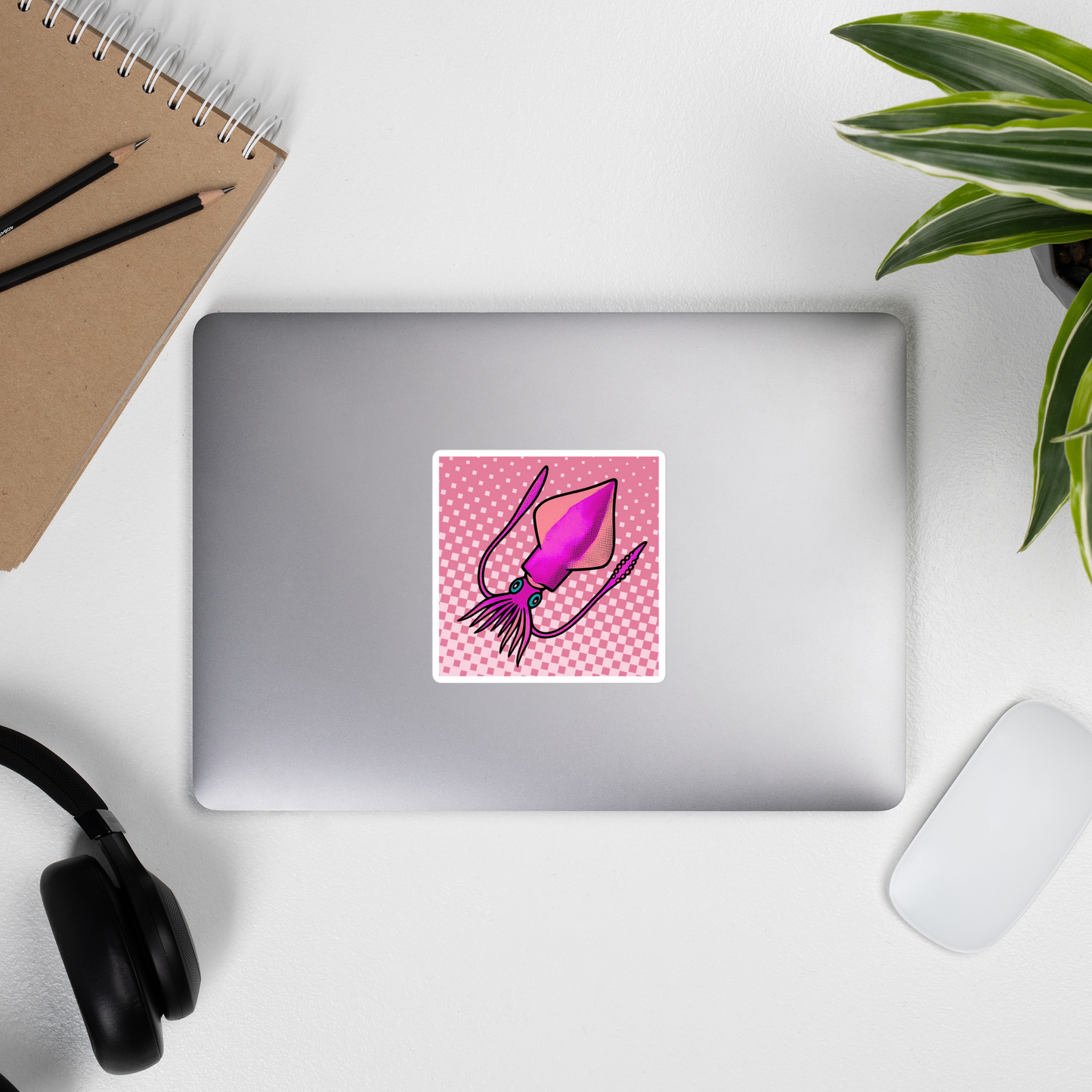 Laptop with a Loligo Vulgaris Squid pop art vinyl sticker 4x4 — pink and magenta squid on a checkered pink background on a white surface with a plant and office supplies.