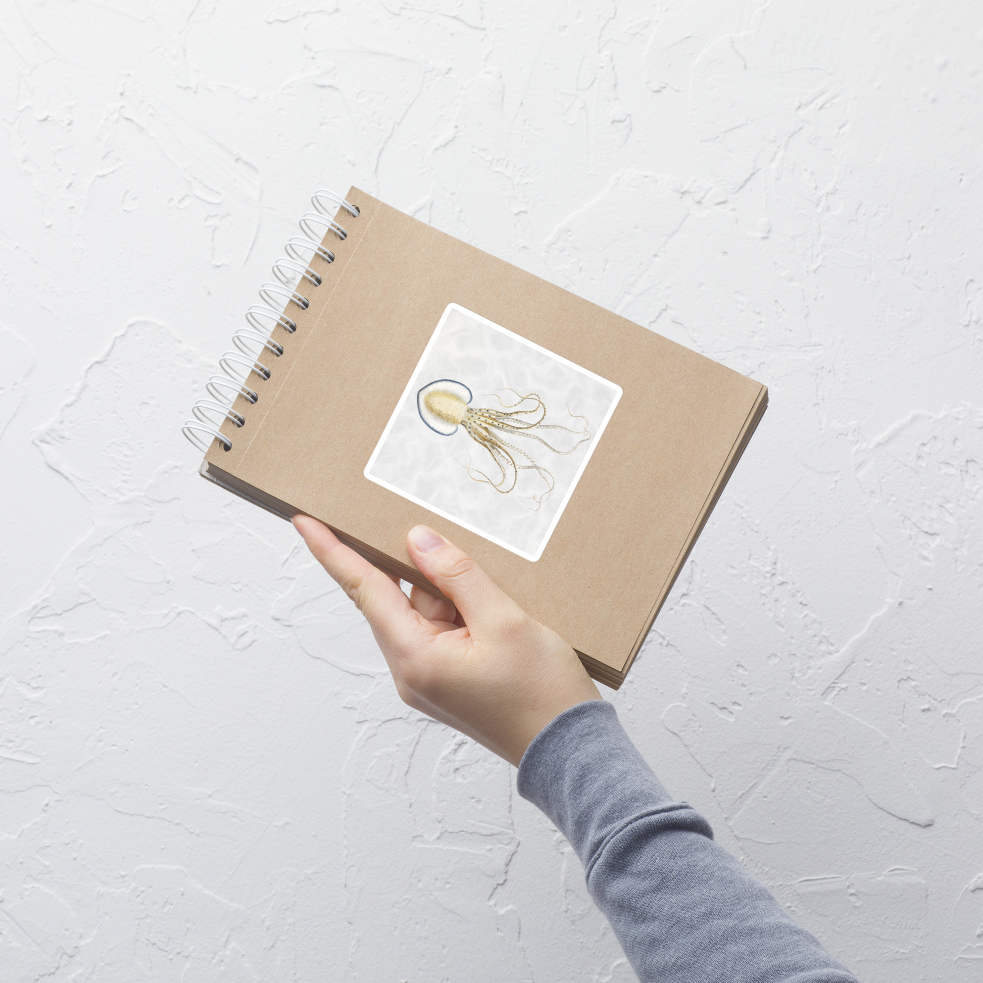 Hand holding a brown notebook with a Pinnoctopus Cordifermis octopus 4x4 vinyl sticker with white background 