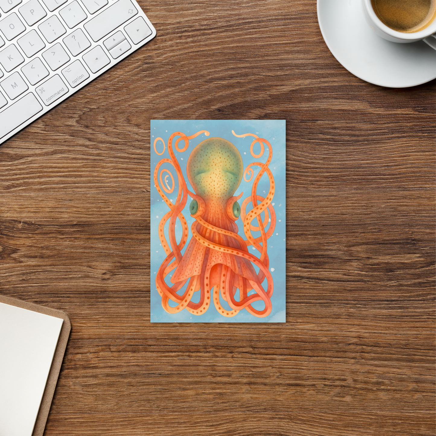 Desk with an 8-Armed Cuttlefish watercolor postcard 4x6 — soft coral and pink cuttlefish with blue ocean wave background on premium cardstock, keyboard, and coffee cup.