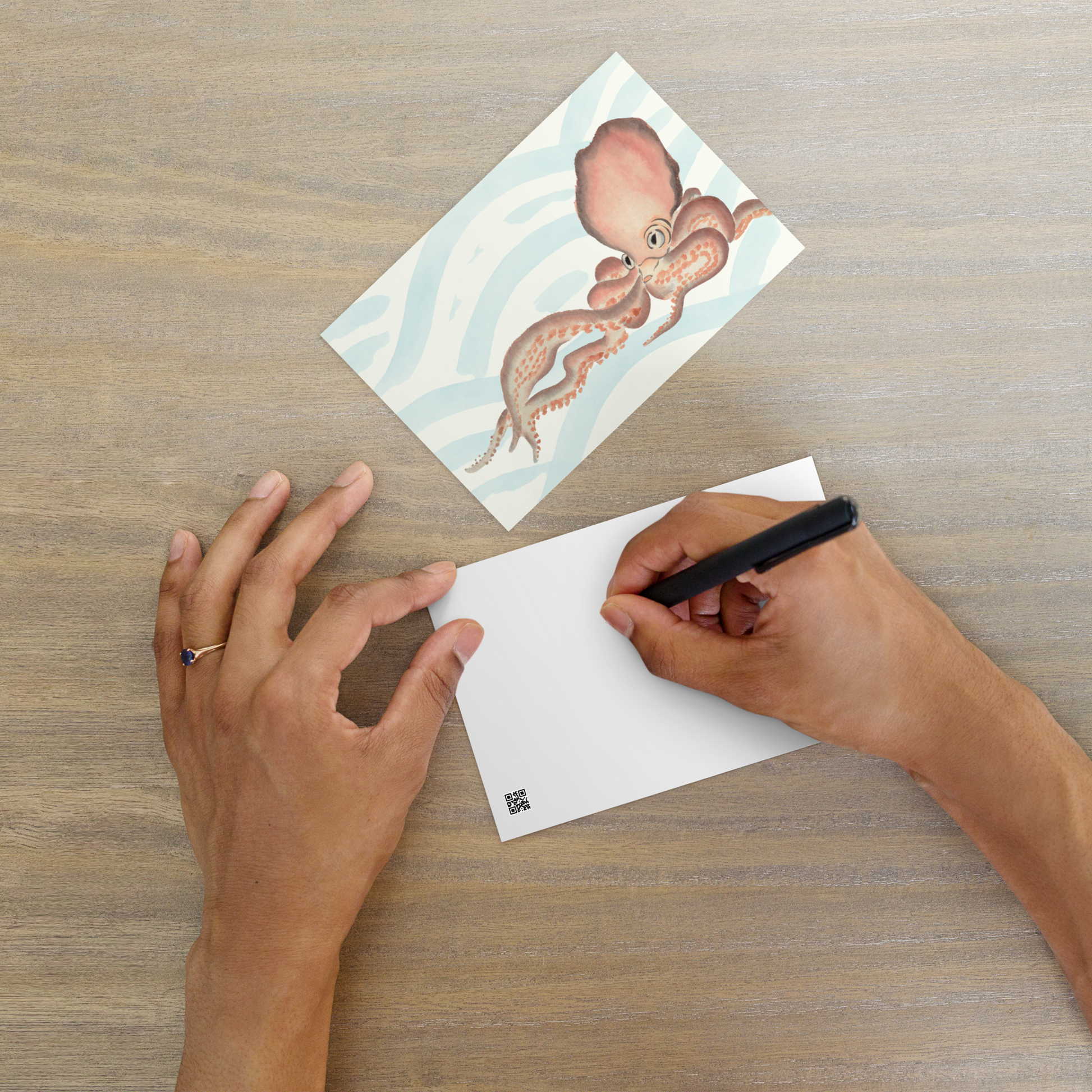 Person writing on a card with a Japanese octopus illustration postcard 4x6 — soft pink watercolor octopus with blue ocean wave background on premium cardstock